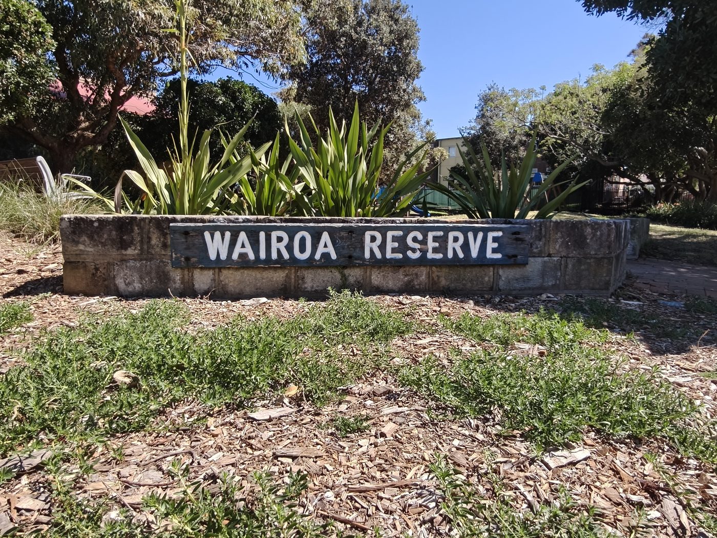 The Wairoa Reserve sign on a sandstone wall, with flax and lilies planted above it